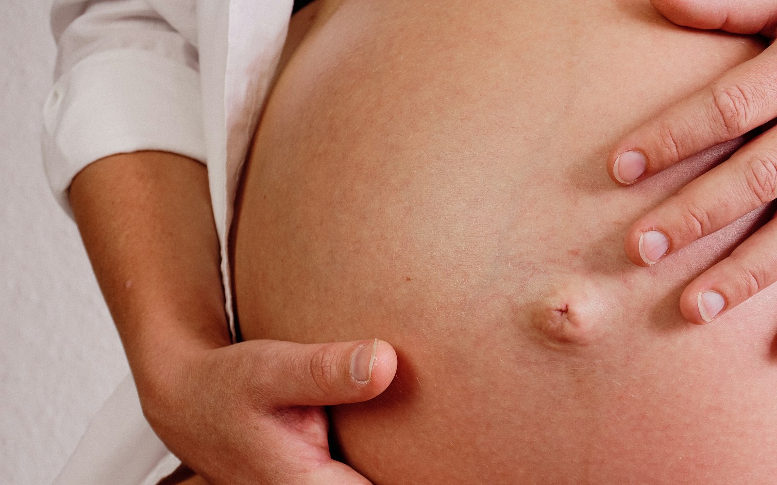 Hands resting gently on a pregnant woman's belly, a reassuring gesture in warm, soft light.