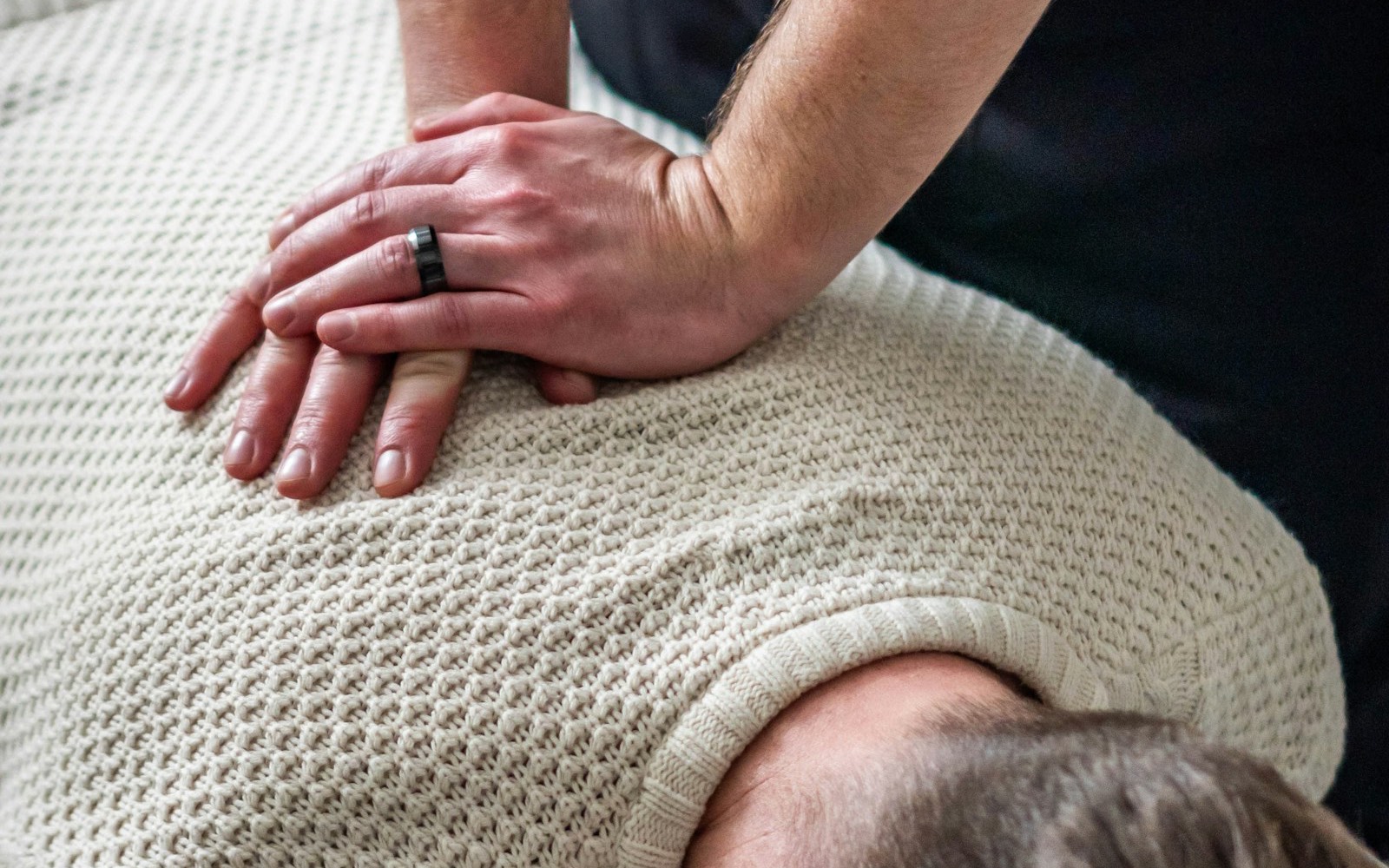 Osteopath applying manual care on the back of a patient lying down, stacked hands, a warm setting.